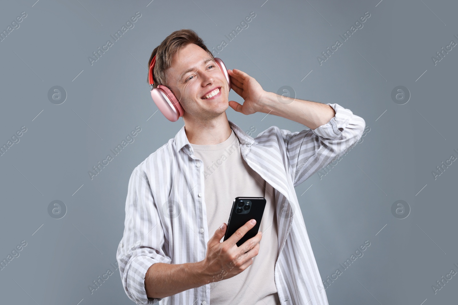 Happy man with smartphone listening to music in headphones on grey background Photo of Happy man with smartphone listening to music in headphones on grey background