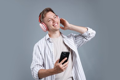 Photo of Happy man with smartphone listening to music in headphones on grey background