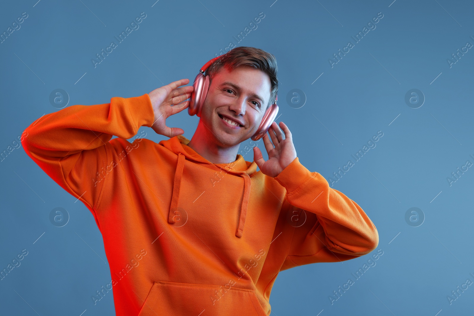 Happy man listening to music in headphones and dancing on blue background Photo of Happy man listening to music in headphones and dancing on blue background
