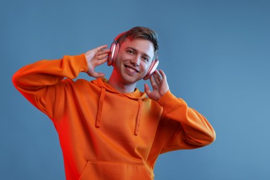Photo of Happy man listening to music in headphones and dancing on blue background