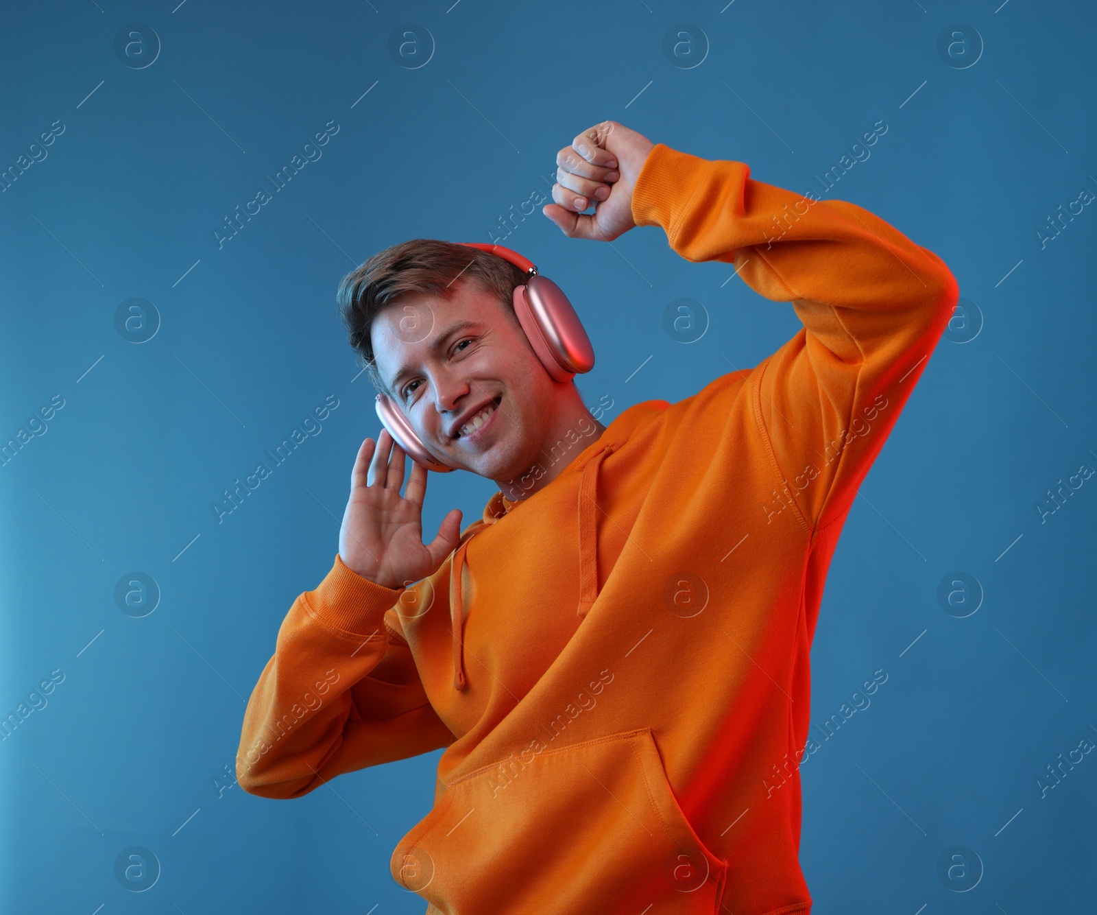 Happy man listening to music in headphones and dancing on blue background Photo of Happy man listening to music in headphones and dancing on blue background