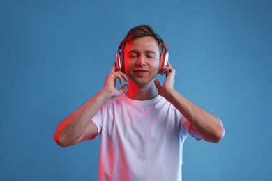Photo of Happy man listening to music in headphones on blue background with neon light