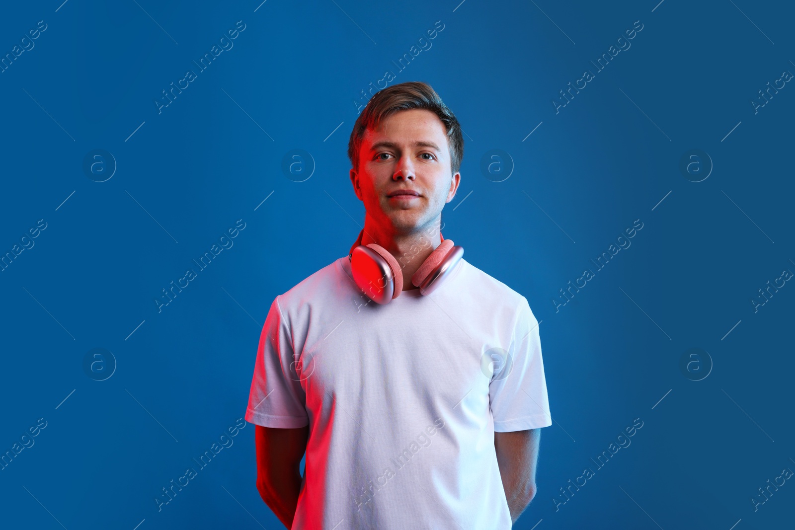 Young man listening to music in headphones on blue background with neon light Photo of Young man listening to music in headphones on blue background with neon light