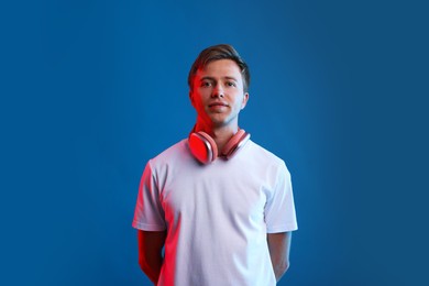 Photo of Young man listening to music in headphones on blue background with neon light