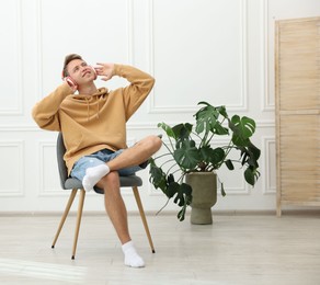 Photo of Happy man listening to music in headphones on chair at home