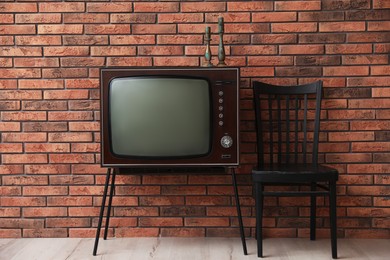 Photo of Retro TV on stand and black chair near red brick wall. Used stuff