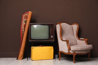 Photo of Retro TV on stand, armchair, suitcase and carpet near brown wall. Used stuff