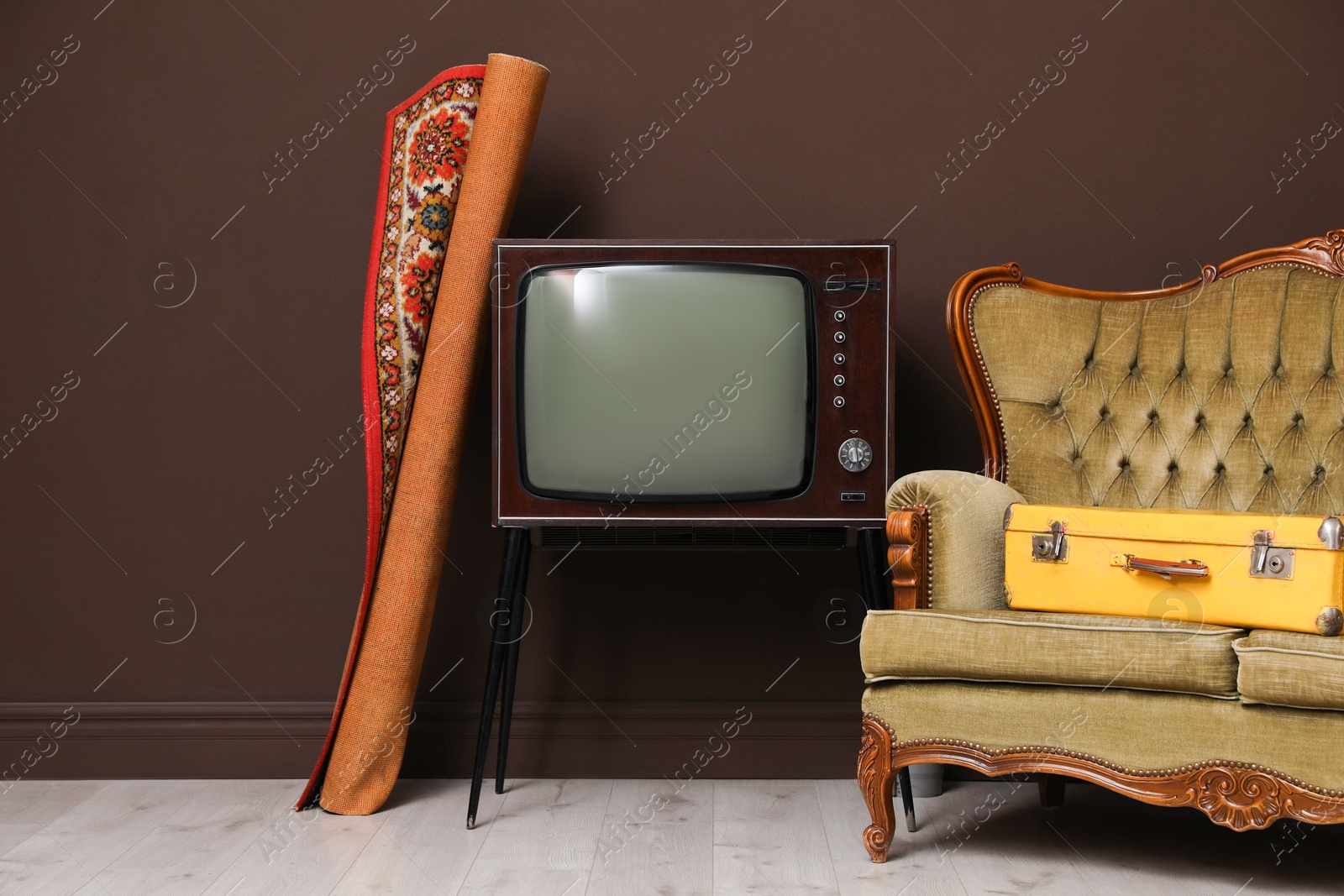 Retro TV on stand, sofa, suitcase and carpet near brown wall. Used stuff Photo of Retro TV on stand, sofa, suitcase and carpet near brown wall. Used stuff