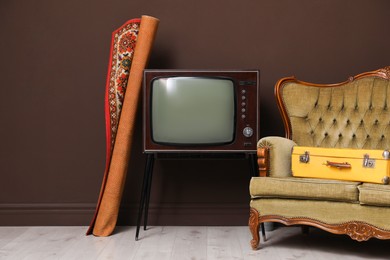 Photo of Retro TV on stand, sofa, suitcase and carpet near brown wall. Used stuff