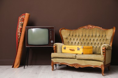 Photo of Retro TV on stand, sofa, suitcase and carpet near brown wall. Used stuff