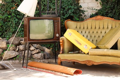 Photo of Retro TV on stand, sofa and other used stuff outdoors