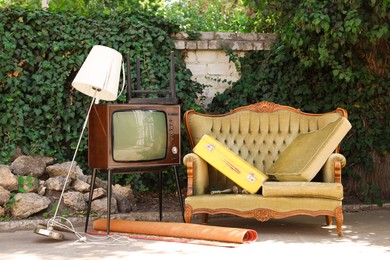 Photo of Retro TV on stand, sofa and other used stuff outdoors