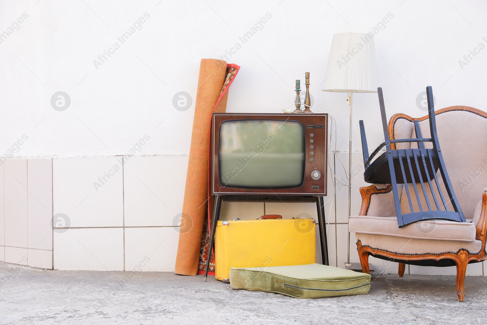 Retro TV on stand, armchair and other used stuff near white wall outdoors. Space for text Photo of Retro TV on stand, armchair and other used stuff near white wall outdoors. Space for text