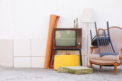 Photo of Retro TV on stand, armchair and other used stuff near white wall outdoors. Space for text