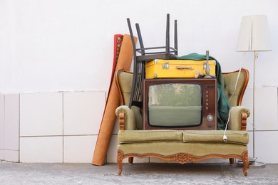 Photo of Retro TV on sofa and other used stuff near white wall outdoors