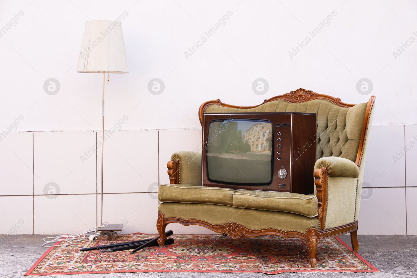 Retro TV on sofa, lamp and carpet near white wall outdoors. Used stuff Photo of Retro TV on sofa, lamp and carpet near white wall outdoors. Used stuff