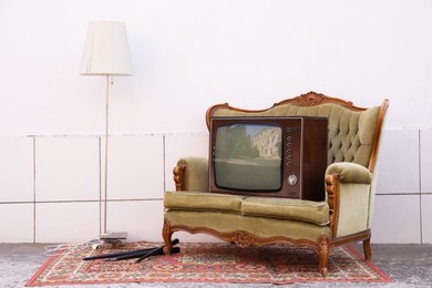 Photo of Retro TV on sofa, lamp and carpet near white wall outdoors. Used stuff