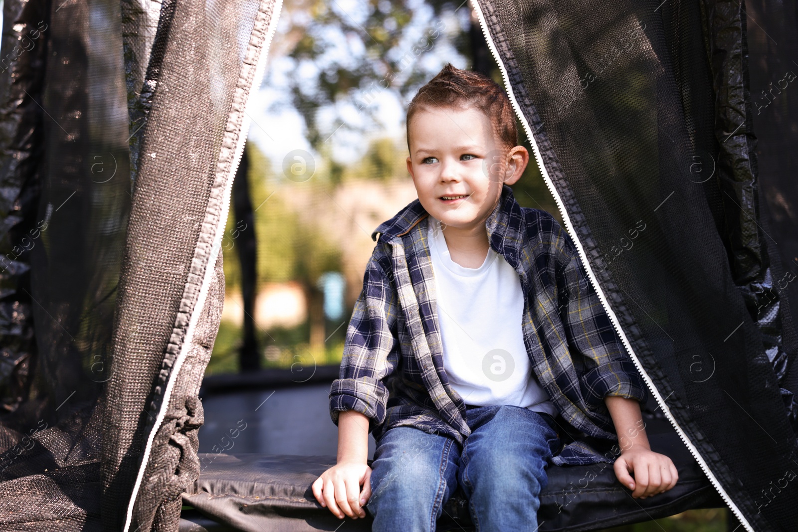 Cute little boy sitting on black trampoline outdoors Photo of Cute little boy sitting on black trampoline outdoors