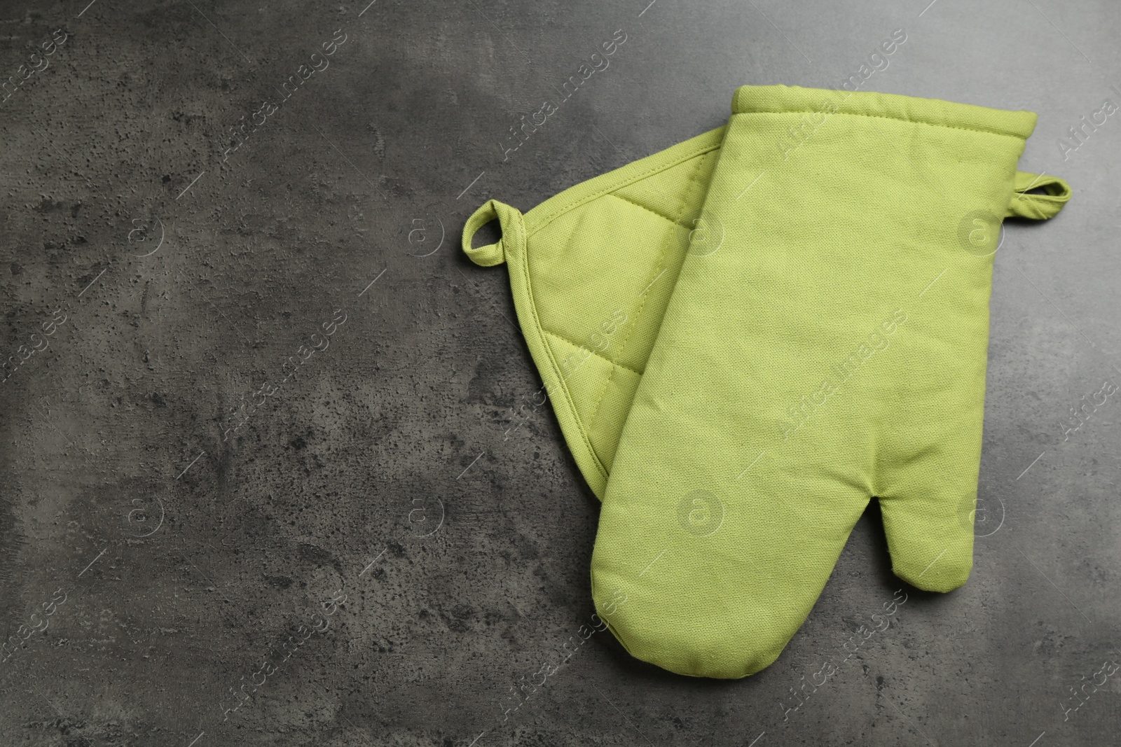 Photo of Green oven glove and potholder on dark textured table, top view. Space for text