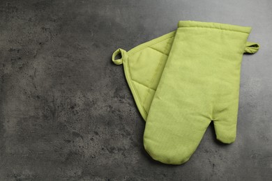 Photo of Green oven glove and potholder on dark textured table, top view. Space for text