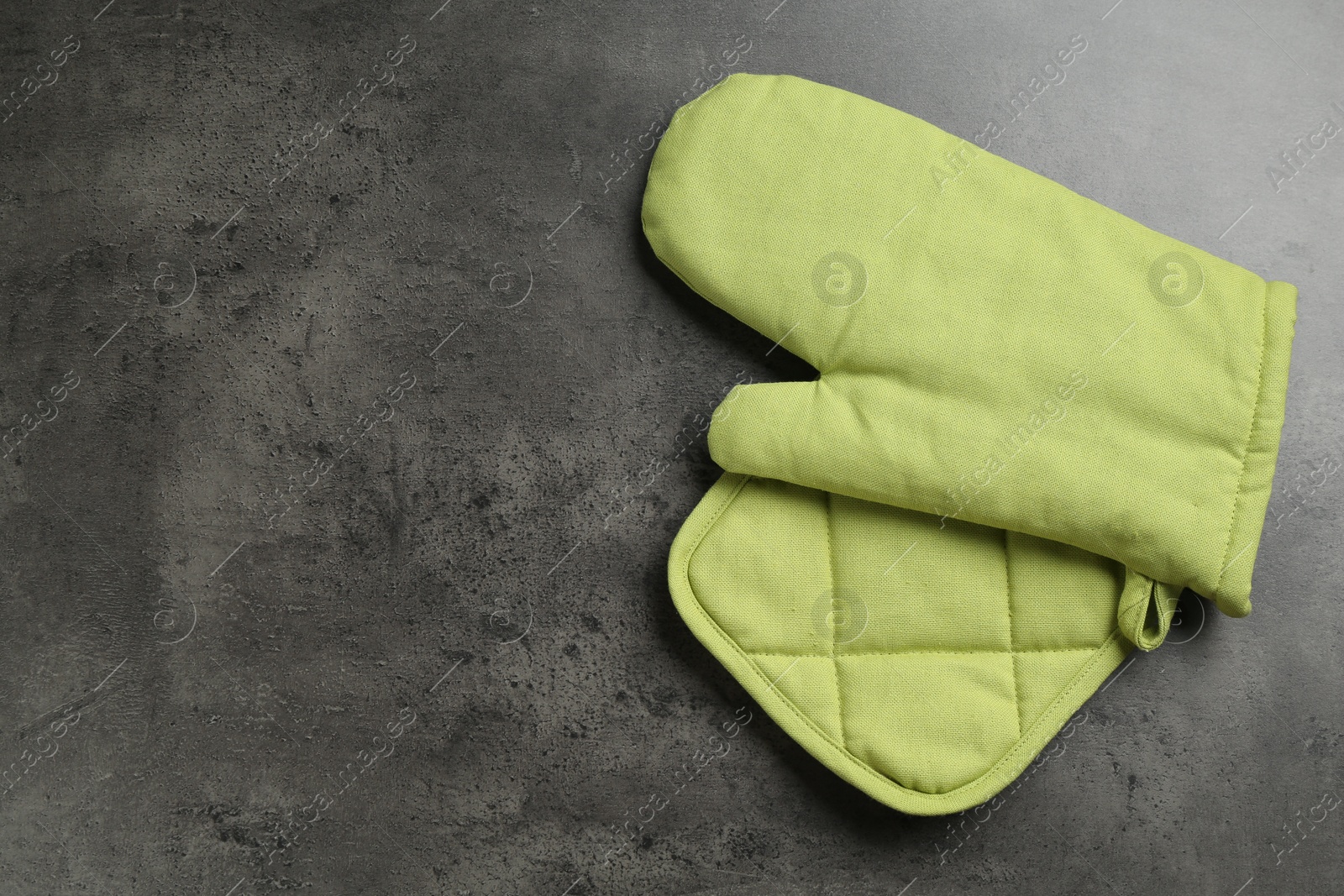 Photo of Green oven glove and potholder on dark textured table, top view. Space for text