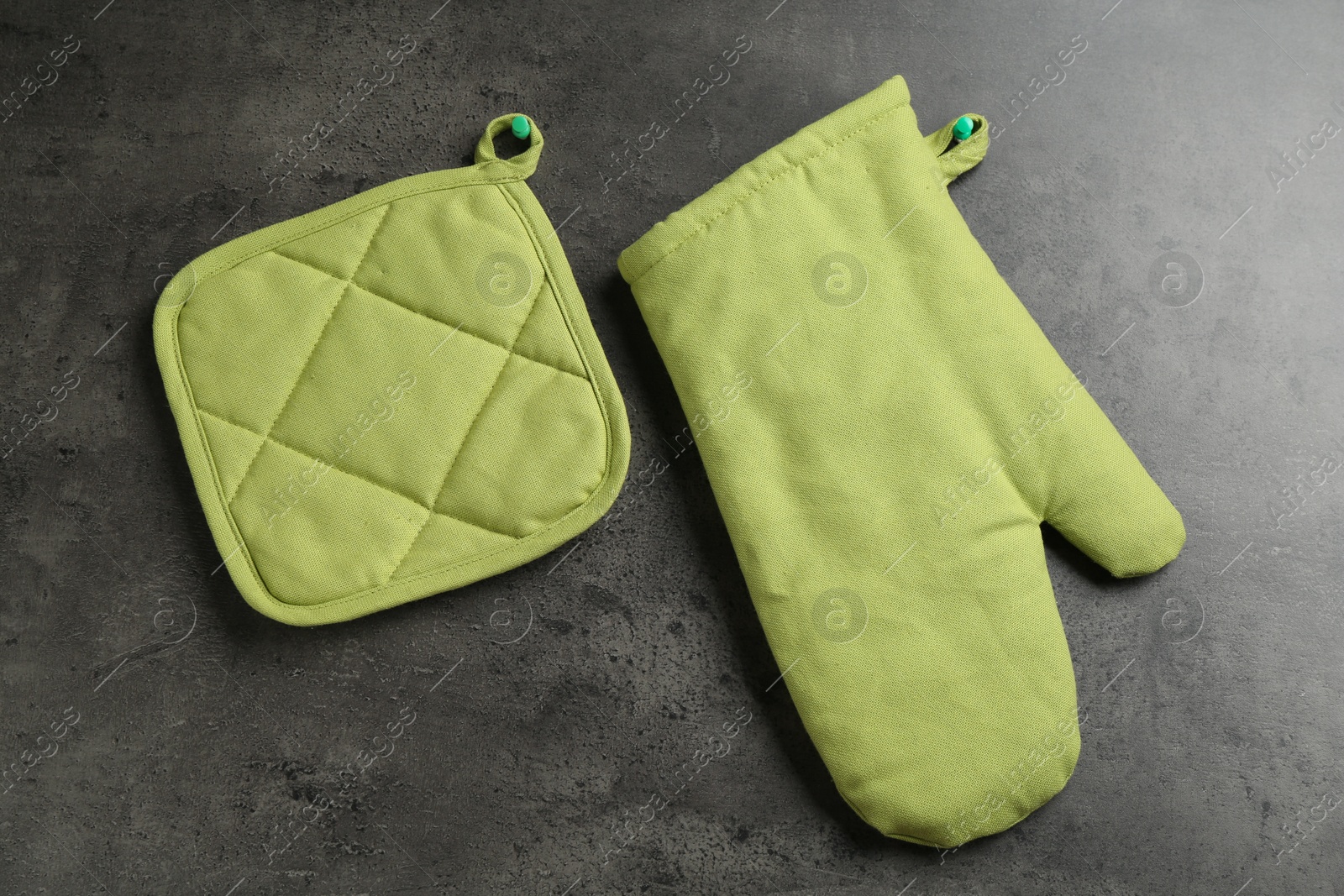 Photo of Green oven glove and potholder on dark textured table, flat lay