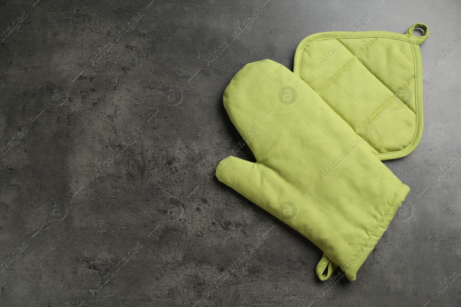 Photo of Green oven glove and potholder on dark textured table, top view. Space for text