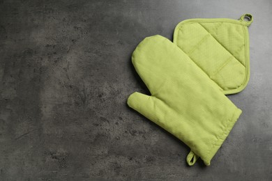 Photo of Green oven glove and potholder on dark textured table, top view. Space for text