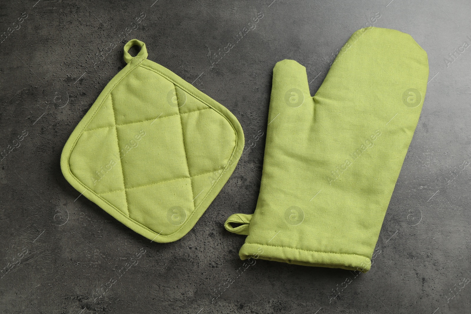 Photo of Green oven glove and potholder on dark textured table, flat lay