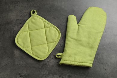 Photo of Green oven glove and potholder on dark textured table, flat lay