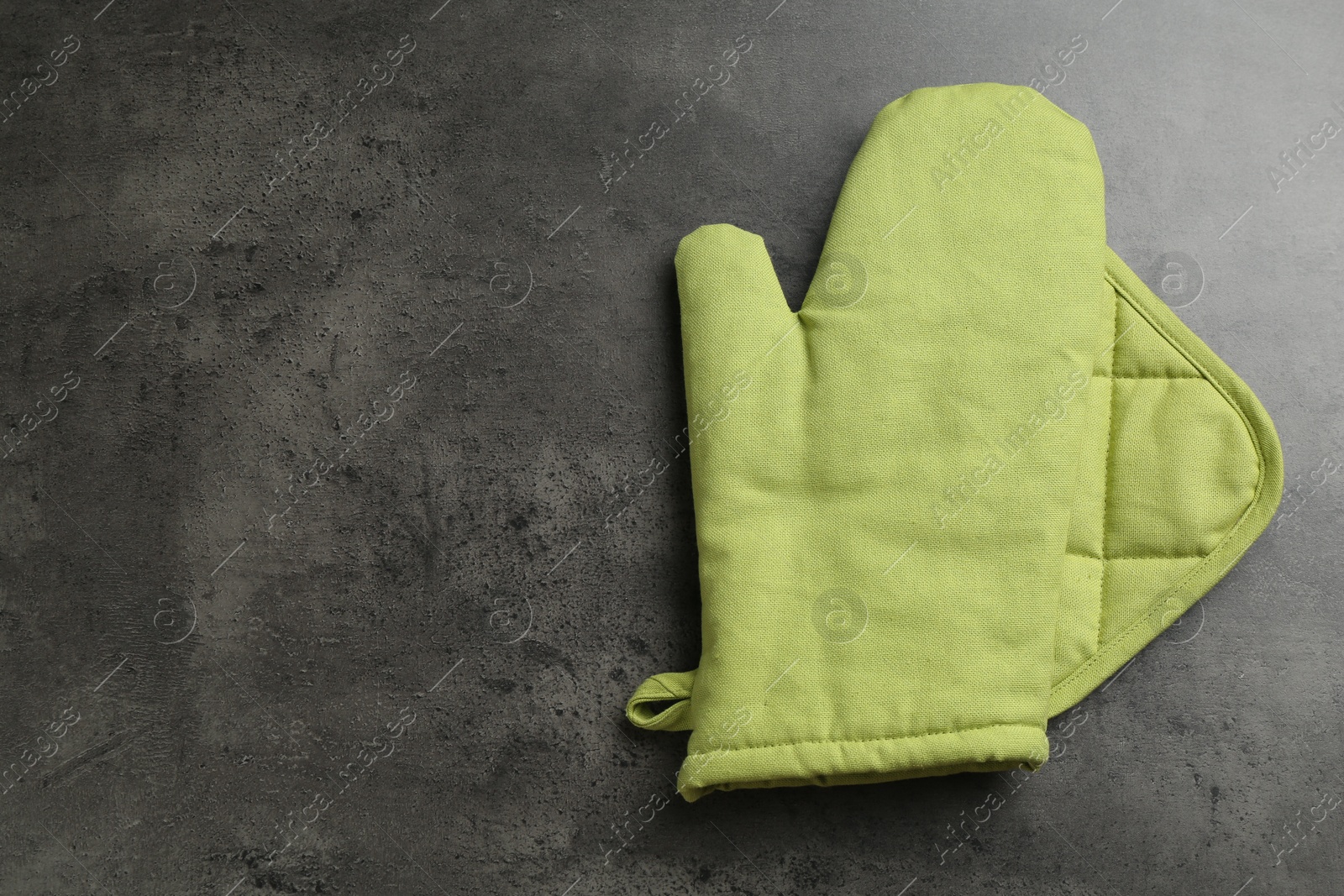 Photo of Green oven glove and potholder on dark textured table, top view. Space for text