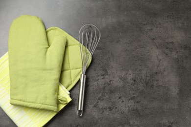 Photo of Green oven glove, potholder, towel and whisk on dark textured table, flat lay. Space for text