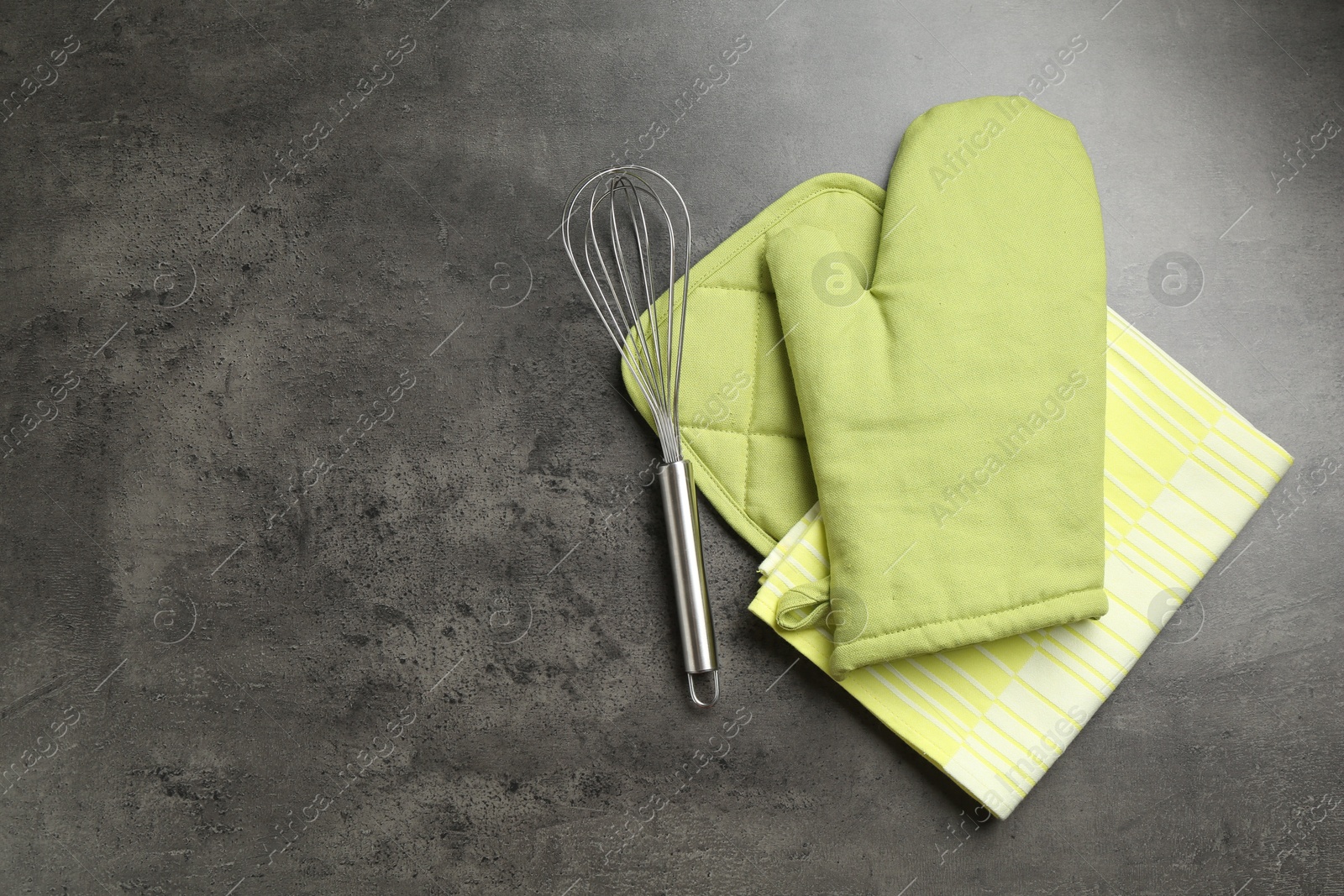 Photo of Green oven glove, potholder, towel and whisk on dark textured table, flat lay. Space for text