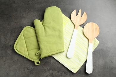 Photo of Green oven glove and other kitchen utensils on dark textured table, flat lay