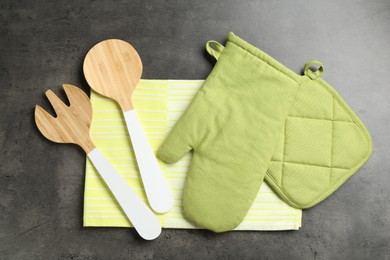 Photo of Green oven glove and other kitchen utensils on dark textured table, flat lay