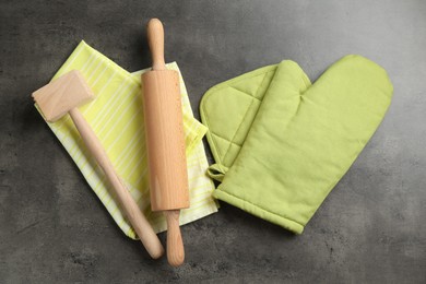 Photo of Green oven glove and other kitchen utensils on dark textured table, flat lay