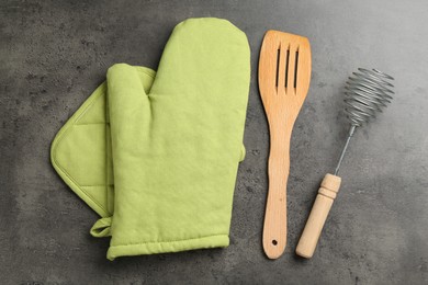 Photo of Green oven glove and other kitchen utensils on dark textured table, flat lay