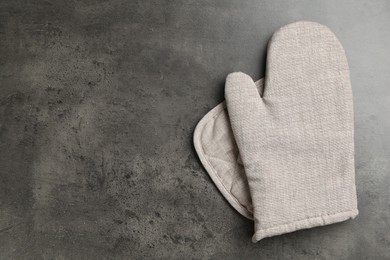 Photo of Grey oven glove and potholder on dark textured table, top view. Space for text