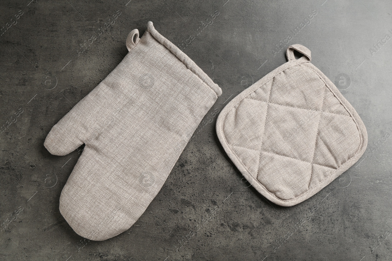 Photo of Grey oven glove and potholder on dark textured table, flat lay