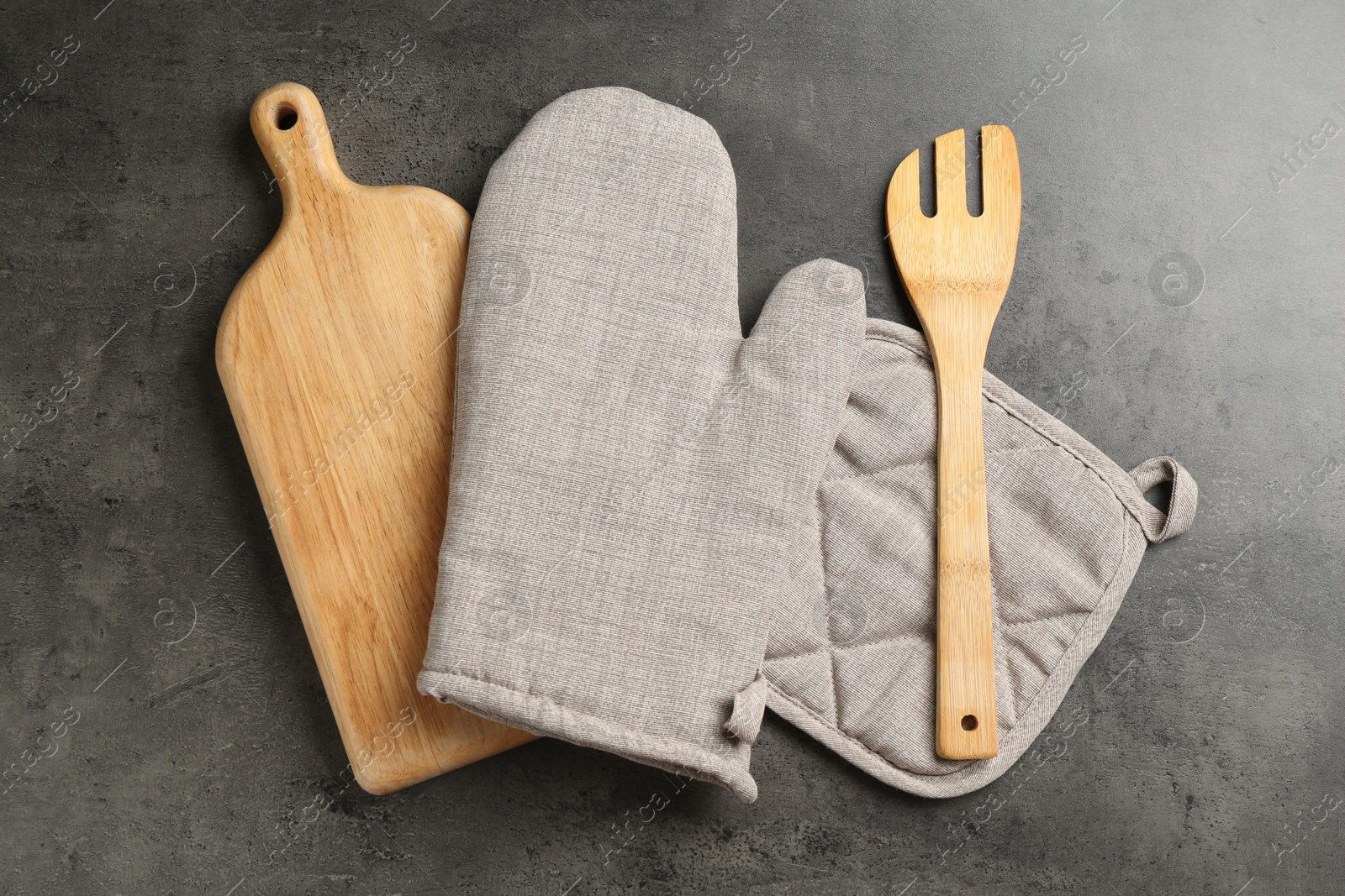Photo of Grey oven glove and other kitchen utensils on dark textured table, flat lay