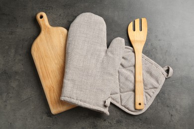 Photo of Grey oven glove and other kitchen utensils on dark textured table, flat lay