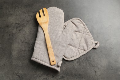 Photo of Grey oven glove, potholder and wooden salad server on dark textured table, flat lay