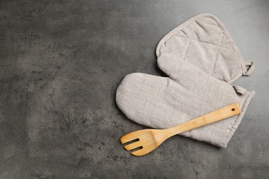 Photo of Grey oven glove, potholder and wooden salad server on dark textured table, flat lay. Space for text
