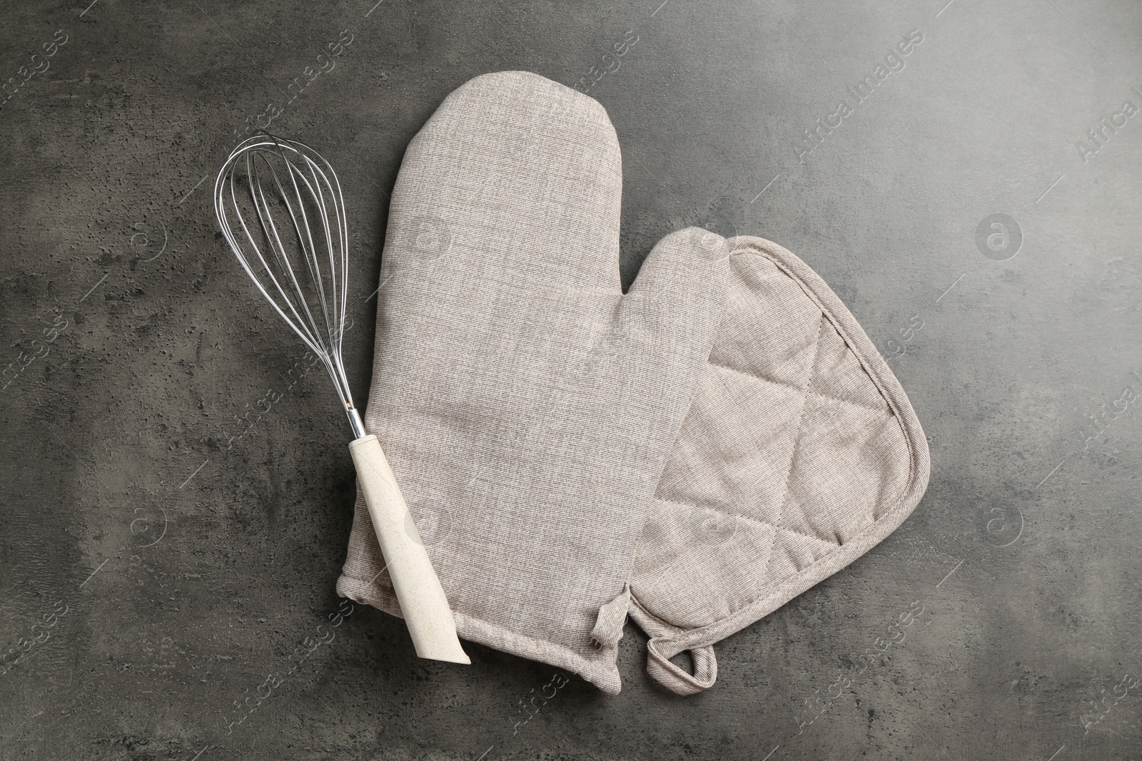Photo of Grey oven glove, potholder and whisk on dark textured table, flat lay