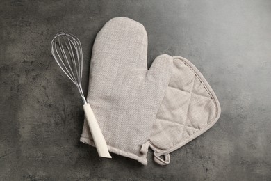 Photo of Grey oven glove, potholder and whisk on dark textured table, flat lay