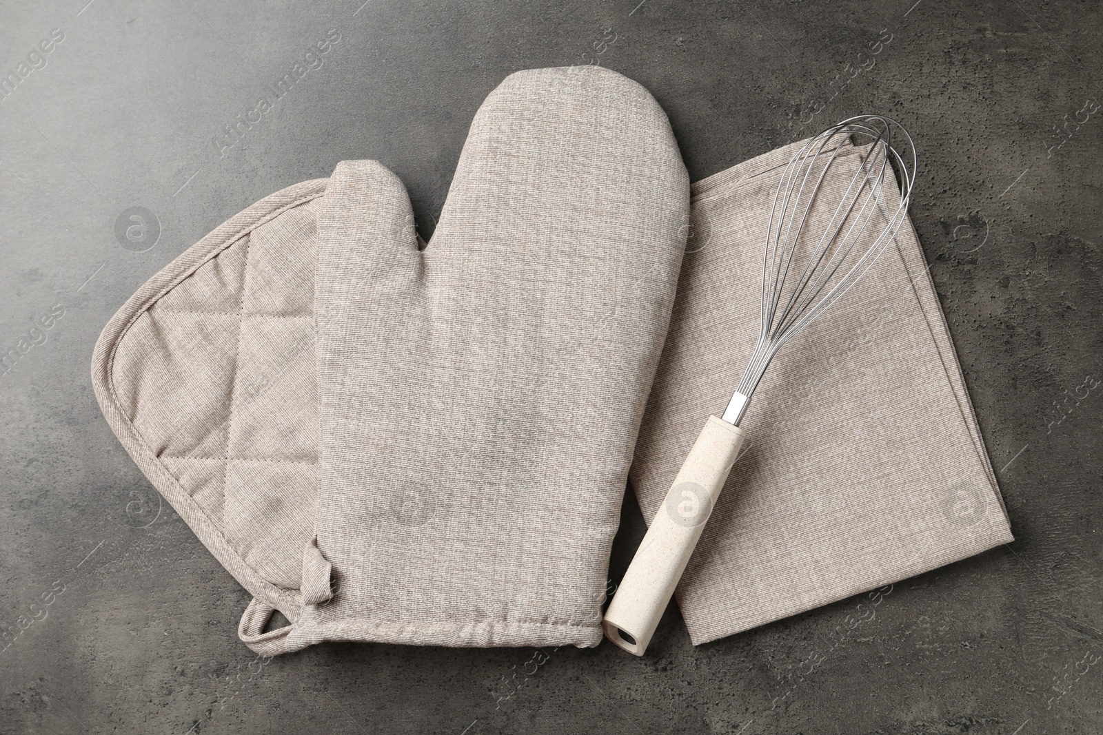 Photo of Grey oven glove, potholder, towel and whisk on dark textured table, flat lay