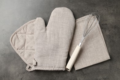 Photo of Grey oven glove, potholder, towel and whisk on dark textured table, flat lay
