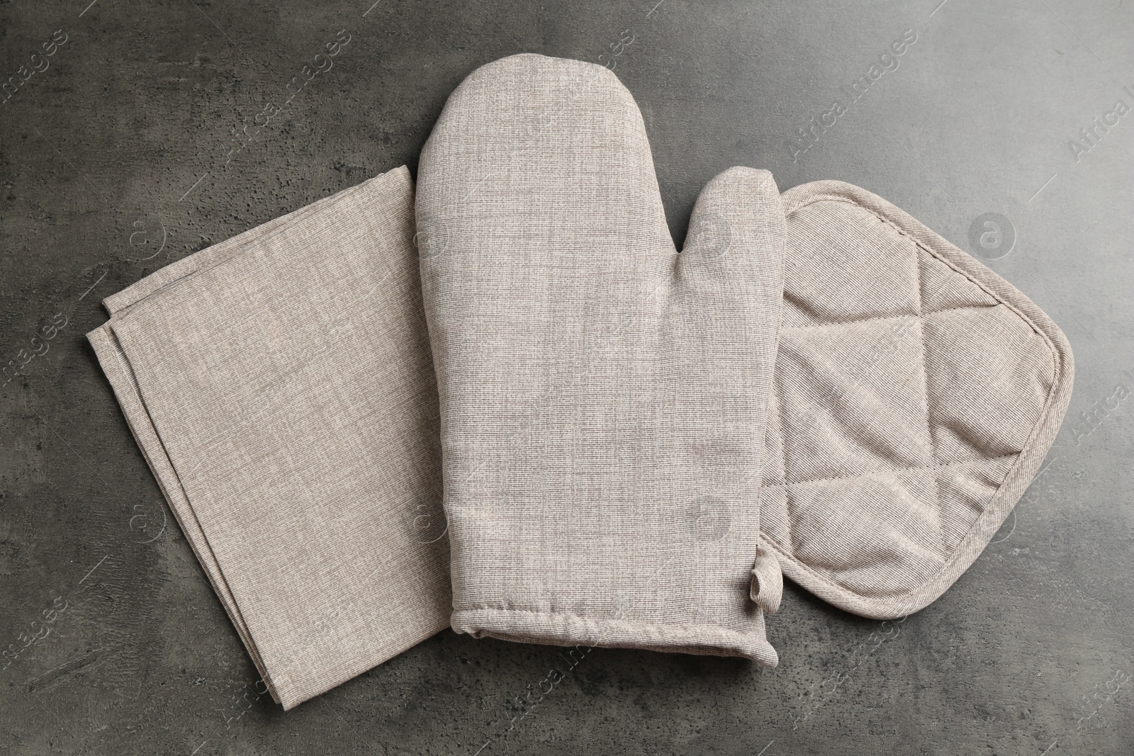 Photo of Grey oven glove, potholder and towel on dark textured table, flat lay