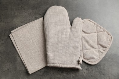 Photo of Grey oven glove, potholder and towel on dark textured table, flat lay