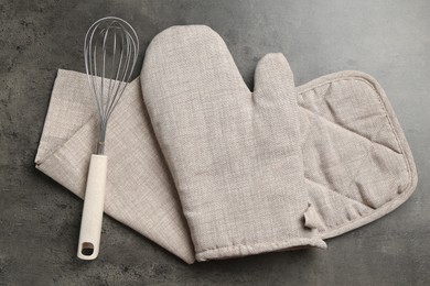 Photo of Grey oven glove, potholder, towel and whisk on dark textured table, flat lay